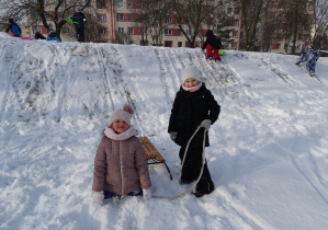 dziewczynka klęczy na śniegu, obok niej druga stoi