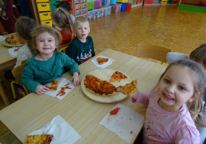 dzieci przy stoliczku jedza pizze