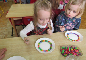 dziewczynki układają kolorowe cukierki na talerzach