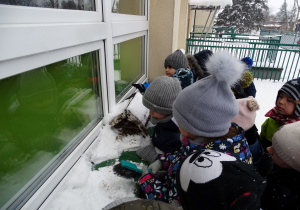 dzieci zgarniają śnieg z okiennego parapetu