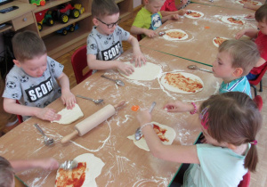 Dzieci nakładają dodatki na pizze.